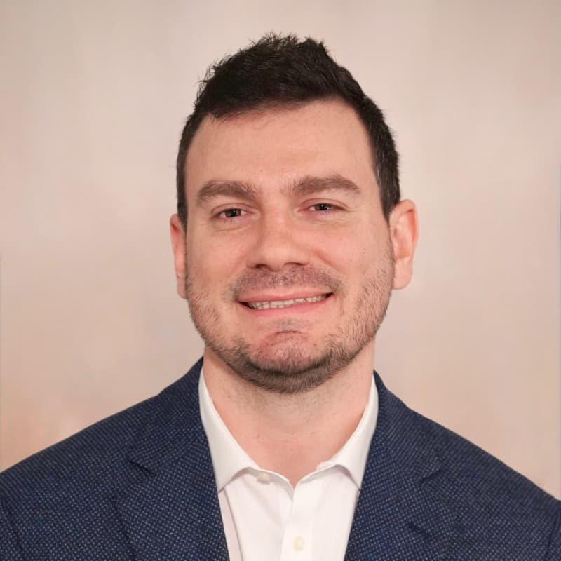 Smiling man with short dark hair and stubble wearing a blue textured blazer.